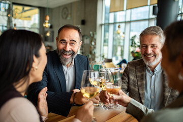 Mature friends laughing and toasting with wine at restaurant