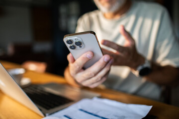 Senior man frustrated with smartphone while paying bills at home
