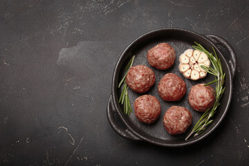 Raw meatballs seasoned with rosemary and garlic are waiting to be cooked in a cast iron pan top view on rustic dark background, copy space