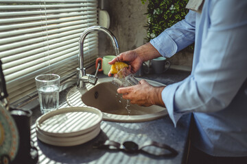 Man washing glass under running water in kitchen sink