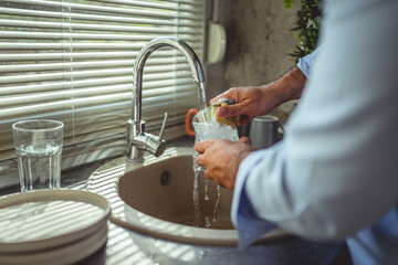 Man washing glass under running water in kitchen sink