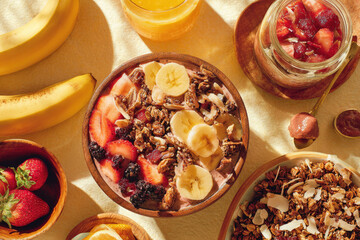 Smoothie bowl with banana strawberry granola coconut and berry surrounded by fresh fruit jam and juice creating vibrant healthy breakfast scene with natural sunlight