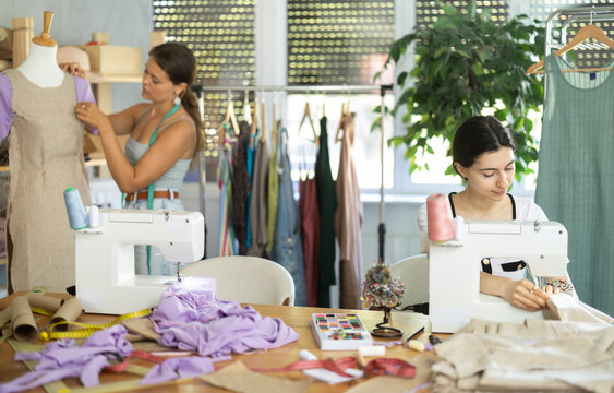 Team of dressmakers works on ordering clothes from a sewing workshop. Fashion designer checks the dress sample on a mannequin, and the seamstress works at the machine