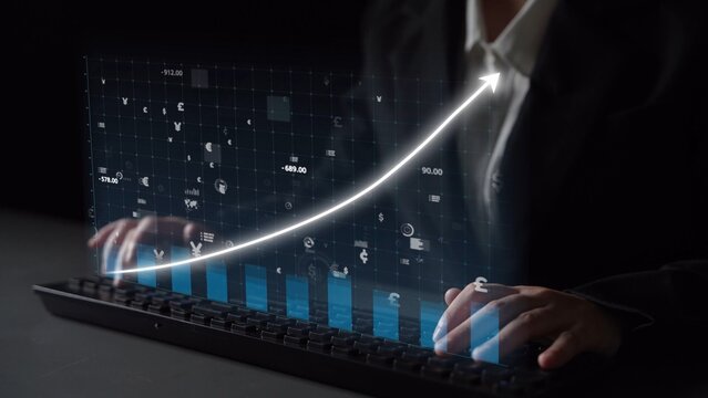 A business professional operates a keyboard as a digital growth chart projects above. This image represents finance, analytics, and technology for investment success. Copula - Powered by Adobe