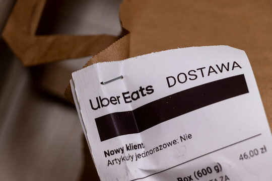 Warsaw, Poland - November 20, 2025: Uber Eats delivery receipt attached to brown paper bag, featuring client details, food packaging, and order confirmation. Efficient online delivery service.