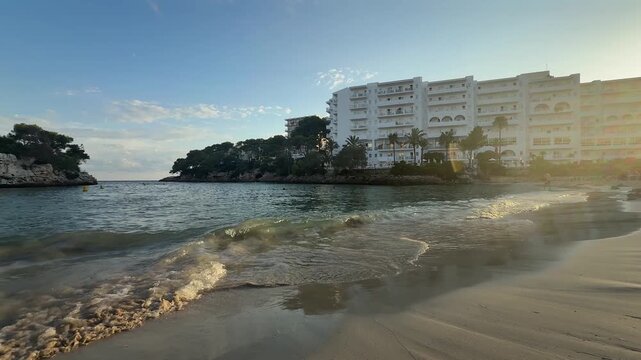 Sunset on Cala Ferrera beach in Cala D'Or village in Mallorca, Spain. Waves playing in sandy bay, warm evening light