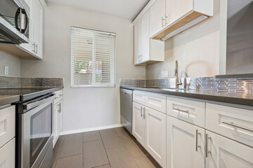 Fototapeta premium A kitchen with white cabinets, stainless steel appliances, and a sink