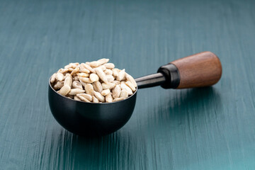 Helianthus annuus - Shelled sunflower seeds in a black spoon with a wooden handle