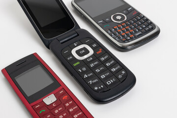 Close-up of three vintage mobile phones from the 1990s isolated on a natural white background, featuring a flip phone and two models with physical keyboards. Retro communication devices concept photo.