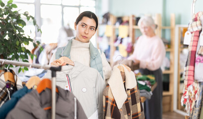 Obraz premium Armenian young girl selecting elegant warm coat or jacket made of high-quality material in big clothes