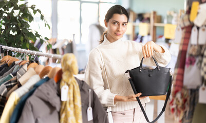 Armenian woman in the store, trying on a fashionable bag, evaluating its comfort and style among the assortment of clothes and accessories