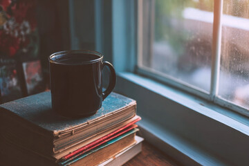 Cup of coffee on stack of vintage books beside window, warm sunlight streaming in, cozy and peaceful morning atmosphere, relaxation and comfort