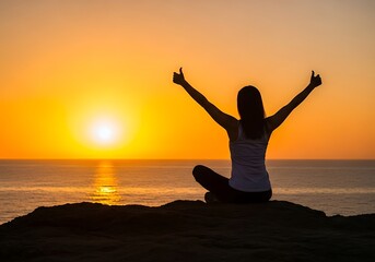 Woman silhouetted in sunset meditating on a rock by the ocean