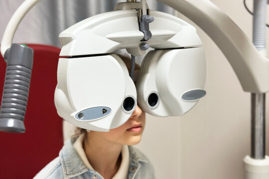Young girl undergoing eye examination with phoropter at optometrist's office
