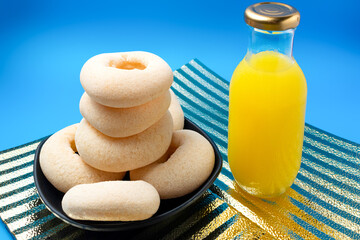Stack of cassava rolls with a bottle of orange juice on a golden plate against a deep blue background.