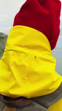 A Young Woman in a Bright Yellow Rain Jacket and Red Beanie Enjoys a Scenic Coastal View, Capturing theBeauty of Nature and Adventure