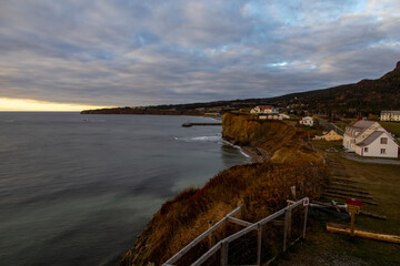 Tranquil dawn over Perce, Quebec, with coastal views, quaint homes, and serene ocean ambiance.
