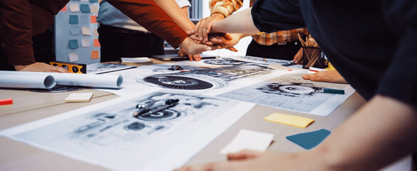 A dynamic creative team engages in a brainstorming session, hands together over design sketches and notes, showcasing collaboration and innovative ideas in an office setting. SACTR