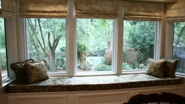 Comfortable window seat with decorative cushions and ornate, patterned fabric provides a cozy indoor space, with views of lush greenery outside the window, evoking relaxation.