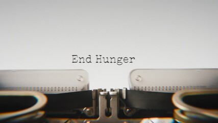 Old mechanical typewriter typing End Hunger in a close-up view, with metal letters striking the white paper.