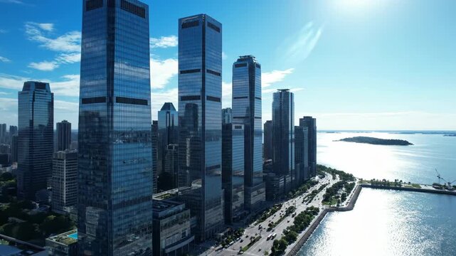 4k, Aerial view capturing a row of modern glass skyscrapers along the waterfront reflecting the clear blue sky with an urban aesthetic and a wide-angle