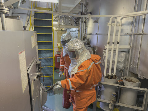 Fire Drill on Cargo Ship Crew Using Firefighting Gear, Breathing Apparatus and Hose During Emergency Training with fire extinguisher near the boiler 16
