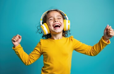 Happy little girl enjoys music with headphones on. She laughs and moves with joy. Girl wears yellow shirt, isolated on blue background. Fun times for kids.