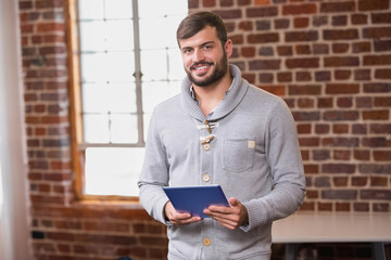 African American man standing by mullioned window in loft holding blue tablet, wearing gray sweater