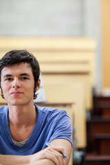 Obraz premium Male in twenties sitting at lecture hall desk wearing blue short-sleeve shirt and holding pen