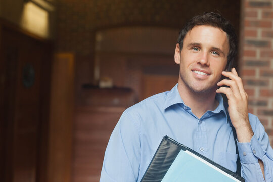 Mid-30s man talking on phone in hall, light-blue shirt, portfolio with blue paper, copy space
