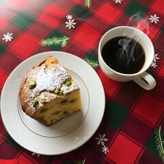 A slice of pistachio cake with powdered sugar and a cup of coffee on a christmas themed tablecloth