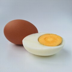 Uncooked and half cut boiled egg. Brown egg and a hard-boiled egg half on a light background. The brown egg is smooth with a uniform color. The boiled egg reveals a white exterior and a yellow yolk.