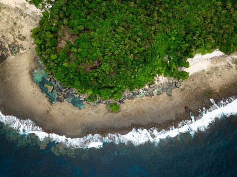 Tidal pools along rocky coastline with dense green tropical forest. Siargao, Philippines.