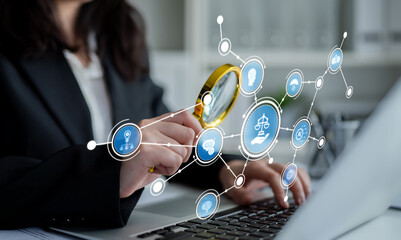 A woman examines legal icons with a magnifying glass while working on her laptop, symbolizing...