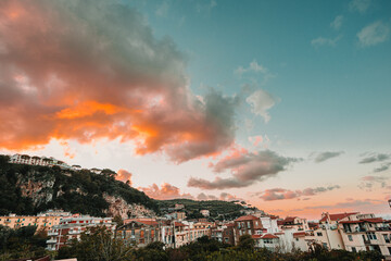 Sunset view over a European hillside town, with buildings nestled among trees under a dramatic sky with orange and pink clouds.