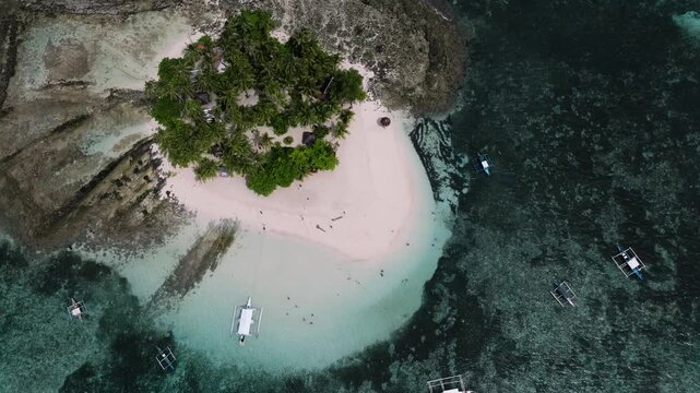 Drone view of island covered with palm trees and white sandy beach surrounded by reef. Guyam Island. Siargao, Philippines.