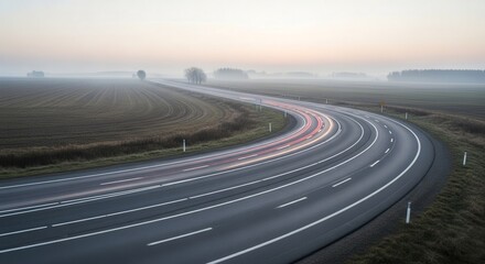 A Misty Morning Drive Along A Winding Road With Car Light Trails And Fields