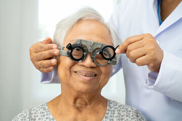 Asian senior woman wearing ophthalmic vision eye test and using optical trial frame.