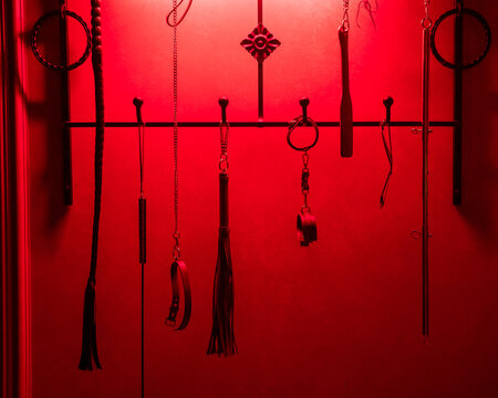 Collection of BDSM toys, whips in red light. 