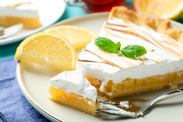 Slice of tasty lemon meringue tart with mint served on blue table, closeup