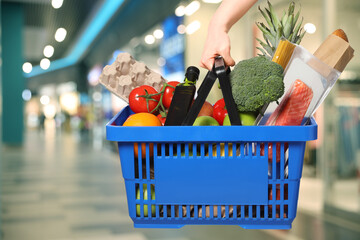 Customer holding shopping basket with different food products at supermarket, closeup