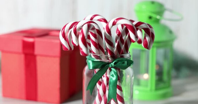 Merry Christmas and Happy New Year. Jar with tasty candy canes, gift box and lantern on white table, closeup. Camera moving right