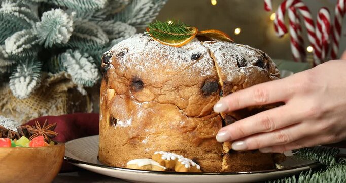 Christmas food. Woman cutting tasty panettone cake at table, closeup. Bokeh effect