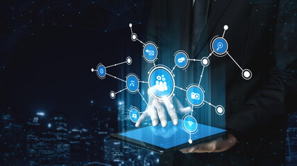 A businessman in a dark suit interacts with a tablet displaying digital network icons. This image represents modern technology, data sharing, and professional communication. Tessel