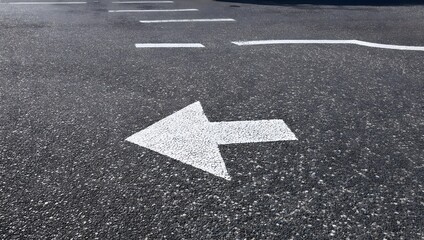 Clean, minimalist shot of a white directional arrow painted on a parking lot floor with gritty asphalt texture. No people, no extra elements.