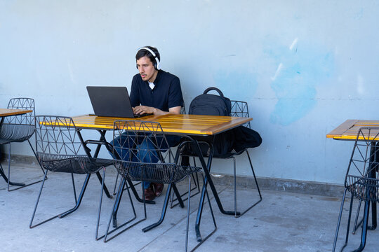 Young man using laptop working at outdoor cafe - Powered by Adobe