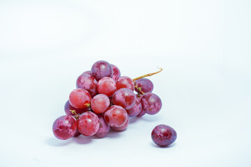Lush bunch of fresh deep red and purple grapes with a single fallen berry on a clean white background, ideal for wine and health themes