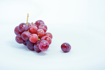 Lush bunch of fresh deep red and purple grapes with a single fallen berry on a clean white background, ideal for wine and health themes