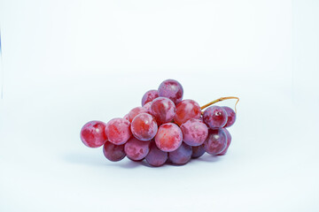 Lush bunch of fresh deep red and purple grapes with a single fallen berry on a clean white background, ideal for wine and health themes