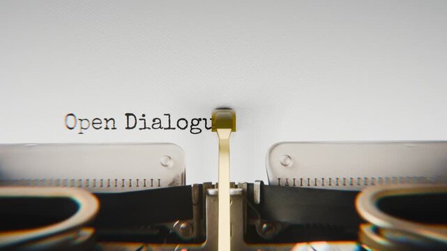 Old mechanical typewriter typing Open Dialogue in a close-up view, with metal letters striking the white paper.